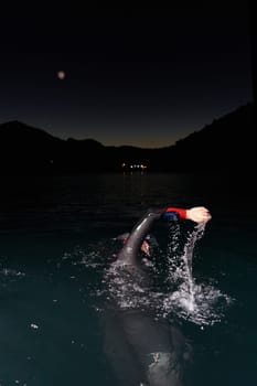 A determined professional triathlete undergoes rigorous night time training in cold waters, showcasing dedication and resilience in preparation for an upcoming triathlon swim competition.