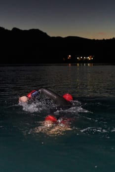 A determined professional triathlete undergoes rigorous night time training in cold waters, showcasing dedication and resilience in preparation for an upcoming triathlon swim competition.