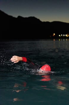 A determined professional triathlete undergoes rigorous night time training in cold waters, showcasing dedication and resilience in preparation for an upcoming triathlon swim competition.