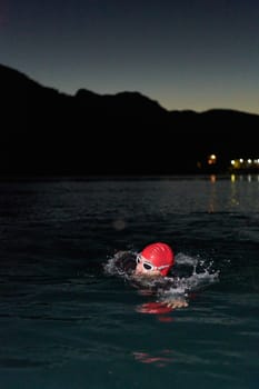 A determined professional triathlete undergoes rigorous night time training in cold waters, showcasing dedication and resilience in preparation for an upcoming triathlon swim competition.