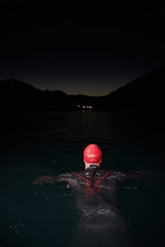 A determined professional triathlete undergoes rigorous night time training in cold waters, showcasing dedication and resilience in preparation for an upcoming triathlon swim competition.