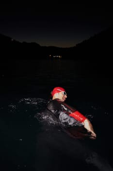 A determined professional triathlete undergoes rigorous night time training in cold waters, showcasing dedication and resilience in preparation for an upcoming triathlon swim competition.