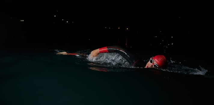 A determined professional triathlete undergoes rigorous night time training in cold waters, showcasing dedication and resilience in preparation for an upcoming triathlon swim competition.