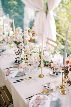 Laid festive table with bouquets of flowers and candles in candlesticks stands on the terrace. High quality photo