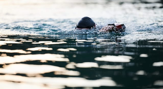 Triathlon athlete swimming on lake in sunrise wearing wetsuit. High quality photo