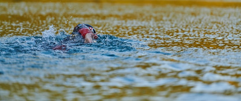 Triathlon athlete swimming on lake in sunrise wearing wetsuit. High quality photo