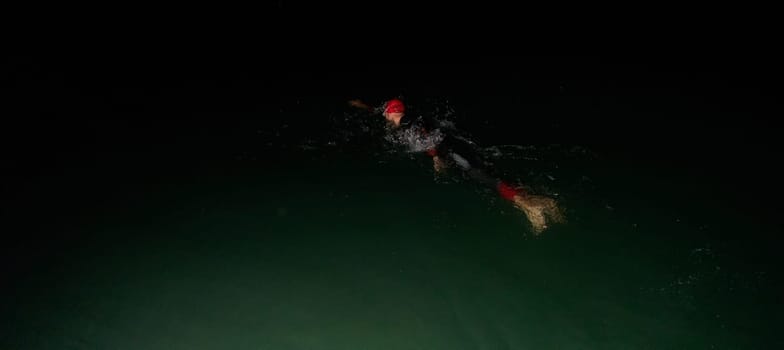 A determined professional triathlete undergoes rigorous night time training in cold waters, showcasing dedication and resilience in preparation for an upcoming triathlon swim competition.