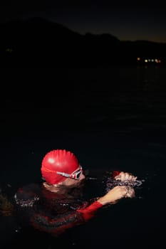 A determined professional triathlete undergoes rigorous night time training in cold waters, showcasing dedication and resilience in preparation for an upcoming triathlon swim competition.