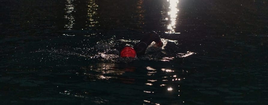 A determined professional triathlete undergoes rigorous night time training in cold waters, showcasing dedication and resilience in preparation for an upcoming triathlon swim competition.