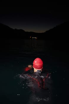 A determined professional triathlete undergoes rigorous night time training in cold waters, showcasing dedication and resilience in preparation for an upcoming triathlon swim competition.