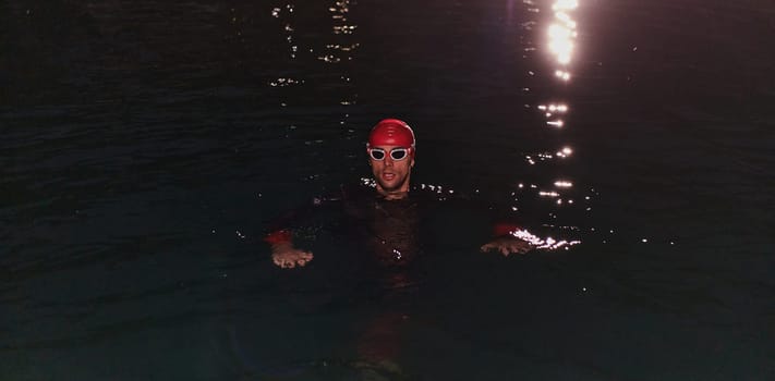 A determined professional triathlete undergoes rigorous night time training in cold waters, showcasing dedication and resilience in preparation for an upcoming triathlon swim competition.