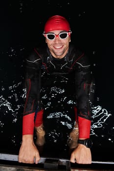 A determined professional triathlete undergoes rigorous night time training in cold waters, showcasing dedication and resilience in preparation for an upcoming triathlon swim competition.