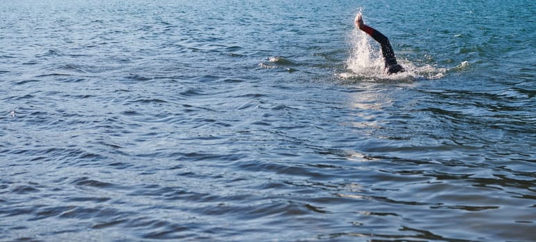 Triathlon athlete swimming on lake in sunrise wearing wetsuit. High quality photo