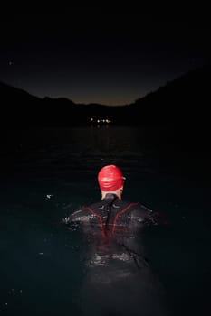 A determined professional triathlete undergoes rigorous night time training in cold waters, showcasing dedication and resilience in preparation for an upcoming triathlon swim competition.