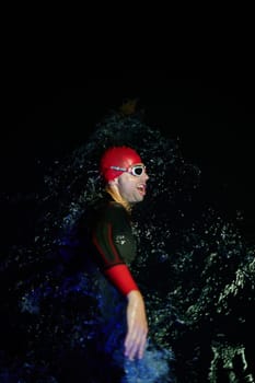 Real triathlete swimmer having a break during hard training at lake on dark night neon gel color lights