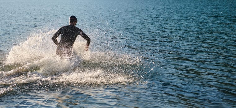 Triathlon athlete starting swimming training on lake.