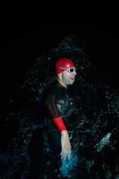 Real triathlete swimmer having a break during hard training at lake on dark night neon gel color lights