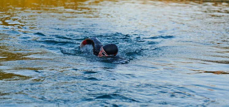 Triathlon athlete swimming on lake in sunrise wearing wetsuit. High quality photo