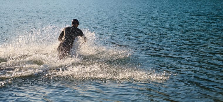 Triathlon athlete starting swimming training on lake.