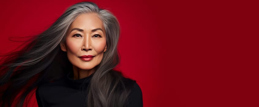 Smiling, elderly, gorgeous Asian woman gray long hair and perfect skin, on a red background, banner. Advertising of cosmetic products, spa treatments, shampoos and hair care products, dentistry and medicine, perfumes and cosmetology for senior women