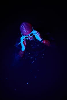 Real triathlete swimmer having a break during hard training at lake on dark night neon gel color lights