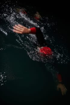 A determined professional triathlete undergoes rigorous night time training in cold waters, showcasing dedication and resilience in preparation for an upcoming triathlon swim competition.