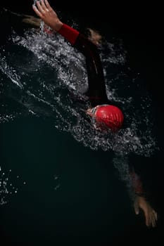 A determined professional triathlete undergoes rigorous night time training in cold waters, showcasing dedication and resilience in preparation for an upcoming triathlon swim competition.