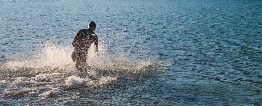 Triathlon athlete starting swimming training on lake.