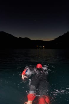 A determined professional triathlete undergoes rigorous night time training in cold waters, showcasing dedication and resilience in preparation for an upcoming triathlon swim competition.