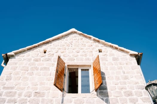 Open wide wooden shutters of the attic window of an ancient stone house. High quality photo