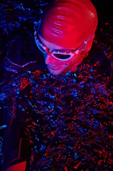 real triathlete swimmer having a break during hard training at lake on dark night neon gel color lights