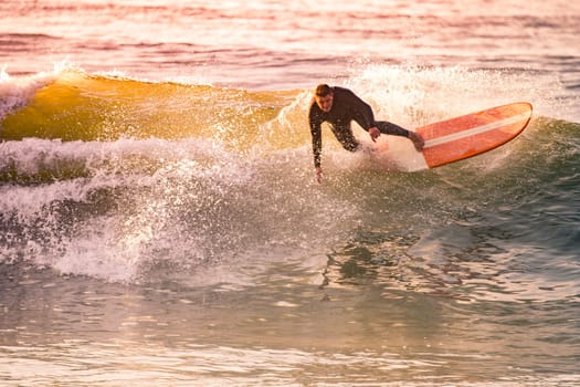 Surfing at Sunset. Young Man Riding Wave at Sunset. Outdoor Active Lifestyle.