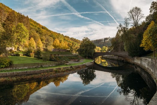 Esch-sur-Sure town situated in picturesque location on bank of Sauer River. Airplane stripes in sky reflected in river of Esch-sur-Sure in Luxemburg