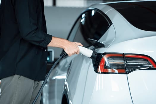 Young man travel with EV electric car to shopping center parking lot charging in downtown city showing urban sustainability lifestyle by green clean rechargeable energy of electric vehicle innards