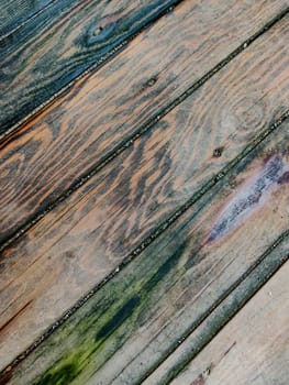 Background of wood coating made of boards with multicolored spots from humidity, diagonal lines, top view, close-up.