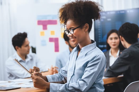 Happy young african businesswoman wearing glasses portrait with group of office worker on meeting with screen display business dashboard in background. Confident office lady at team meeting. Concord