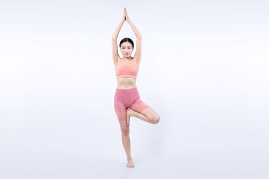 Asian woman in sportswear doing yoga exercise in standing pose on fitness as her workout training routine. Healthy body care and meditation yoga lifestyle in full shot on isolated background. Vigorous