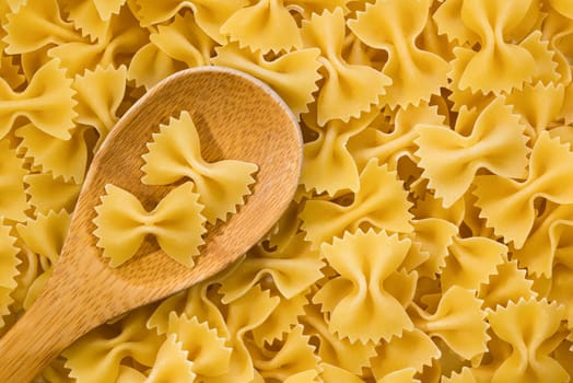 Raw farfalle pasta and wooden spoon, closeup. Top view.