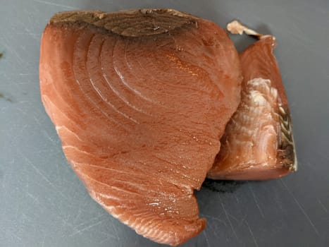Two fresh fish fillets on a gray surface, ready to be cooked. The fillets are pink in color and have a shiny texture. The fillets are cut in a way that they are ready to be cooked. The background is a gray surface, possibly a kitchen countertop.
