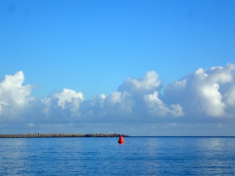 A view of Kahului Harbor in Maui, Hawaii with a red buoy in the foreground and a breakwater in the background.