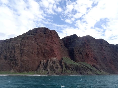 The Na Pali Coast on Kauai, a rugged and scenic stretch of coastline with red cliffs, green vegetation, and blue ocean.