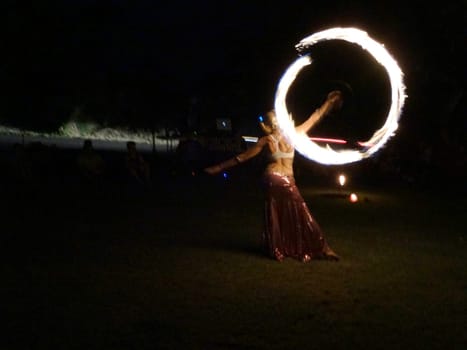 Maui - November 5, 2016:  Fire dancer performing at night at the Maui Yoga Festival. The dancer is holding a flaming hoop and wearing a red and gold outfit. The photo shows the movement and skill of the dancer, as well as the festive atmosphere of the event.