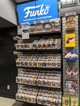 Honolulu - November 5, 2021: Funko Pop! figures inside a GameStop store. The display is against a black wall with a blue Funko logo above it. The display consists of multiple shelves with Funko Pop! figures of various characters from different franchises. There are also some other merchandise on the shelves, such as a Funko Pop! t-shirt and a Funko Pop! keychain.