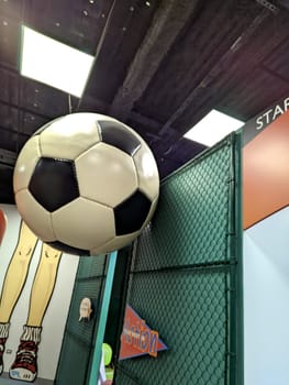 Honolulu - October 7, 2022: Oversized soccer ball hanging from the ceiling of the Children's Discovery Center on Oahu, Hawaii. The soccer ball is black and white and made of a shiny material. The photo shows the "Action Station" sign and a mural of a cartoon character in the background. The photo is taken from a low angle, looking up at the ball.