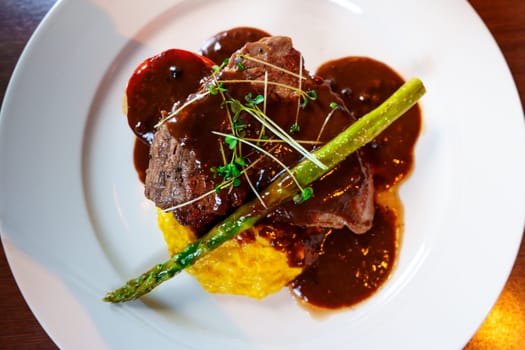 Indulge in the luxury of dining with a delectable combination of juicy steak, velvety mashed potatoes, tender asparagus, and flavorful sauce perfectly presented on a clean white plate.