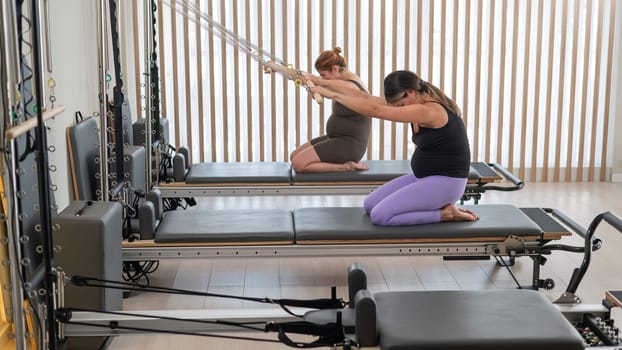 Two pregnant women do Pilates exercises on a reformer