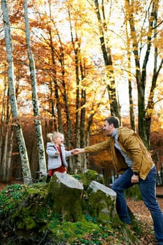 Dad extends his hand to a little laughing girl standing on stumps in the forest. High quality photo