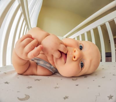 A playful baby in the crib, gleefully staring at the camera, radiating joy.