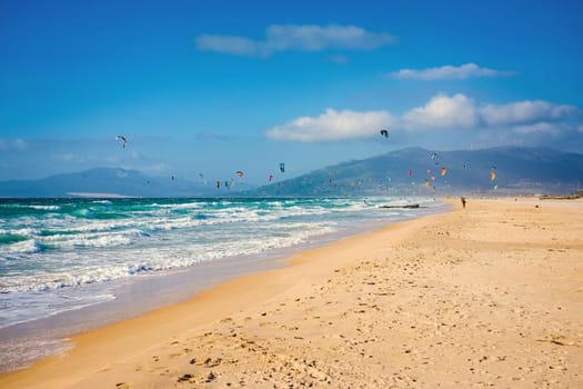 Soaring kite surfers and beach with Atlantic ocean and golden sand on background of mountains. Spain Tarifa