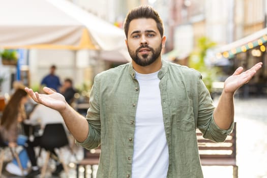 I dont know what to say. Confused young man feeling embarrassed about ambiguous question, having doubts, no idea, being clueless uncertain outdoors. Caucasian adult guy standing in urban city street